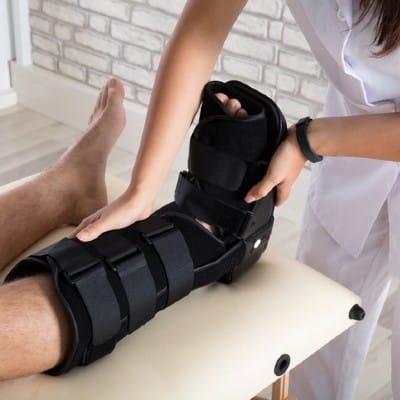 A medical professional fits a leg brace for a patient during orthopedic therapy, supporting joint recovery