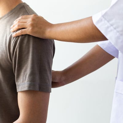 A sports medicine expert evaluates a patient’s back and shoulder during an orthopedic exam for musculoskeletal and spine-related conditions.