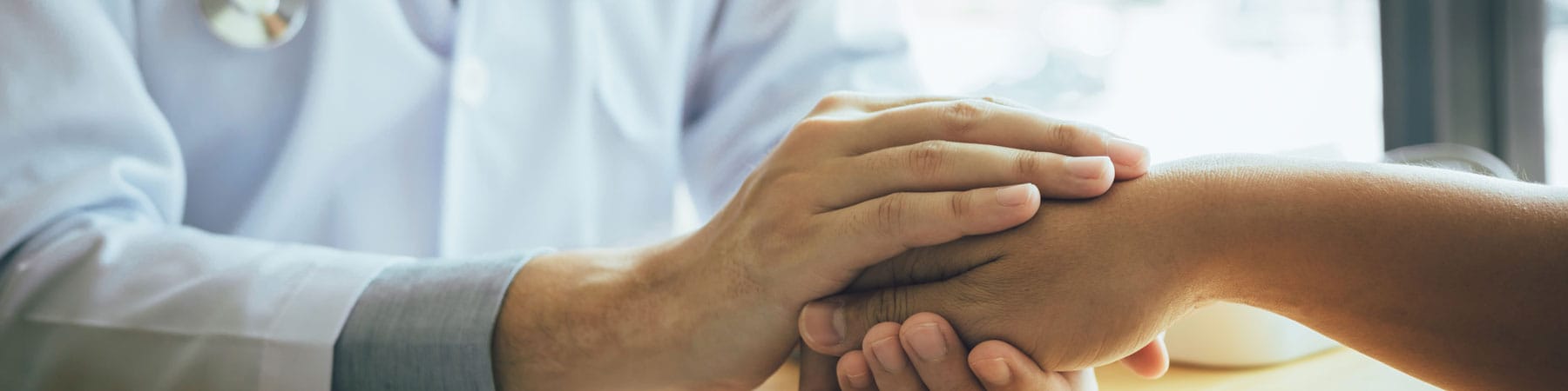 A doctor holds a patient's hand, representing compassionate orthopedic care and patient support through the Advanced Orthopedics patient portal for appointments and bill pay.